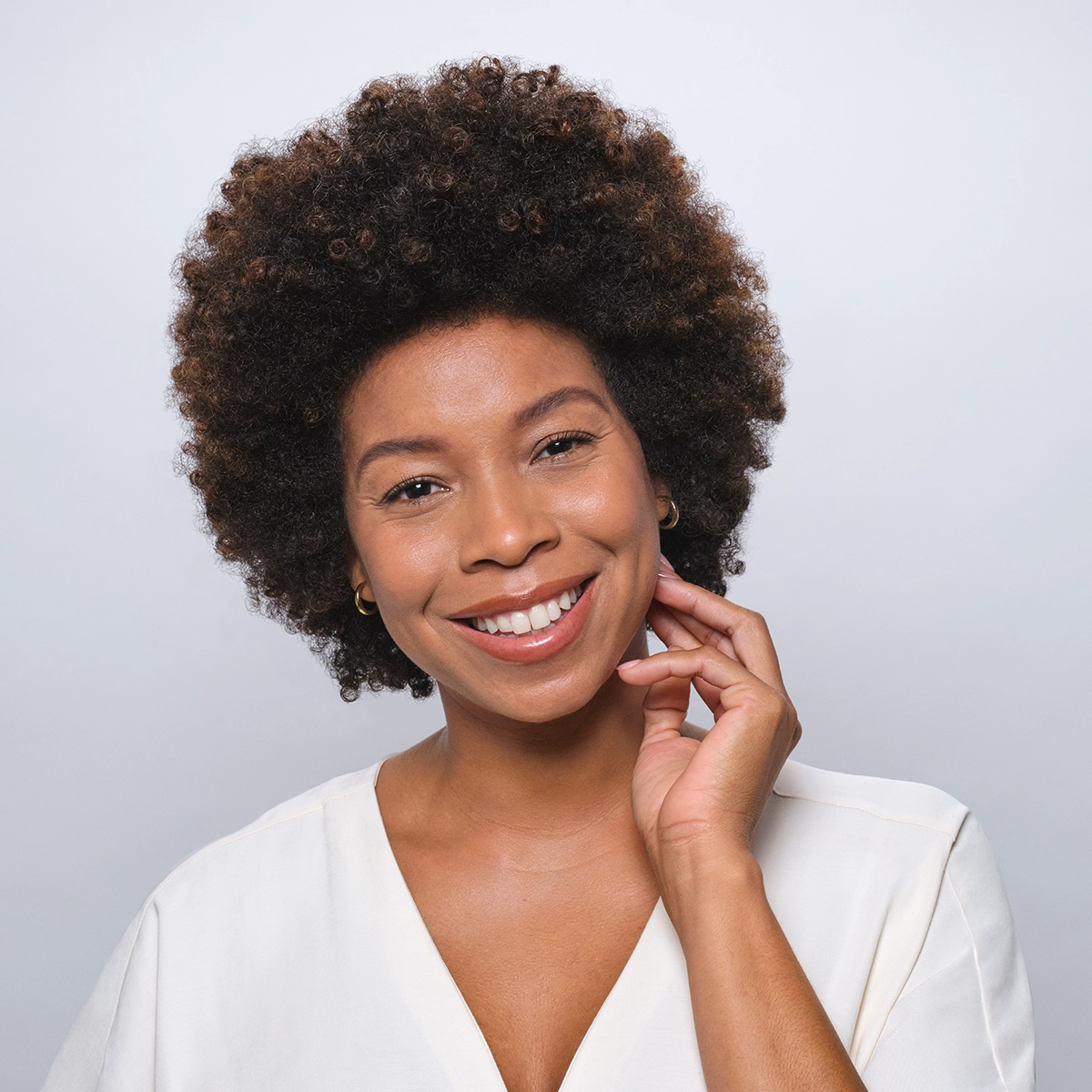 Woman touching face and smiling showing healthy-looking skin.