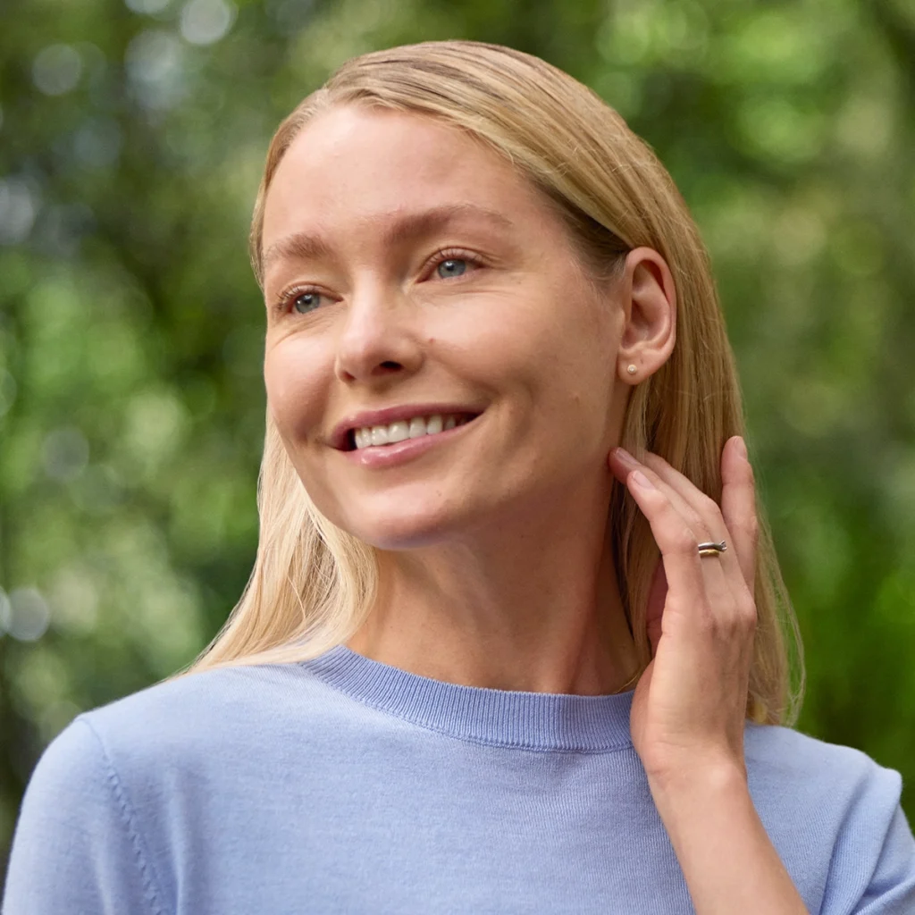 Woman outdoors smiling and touching her face